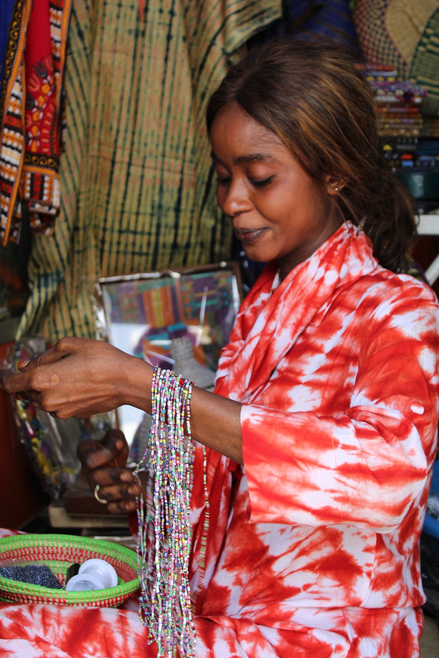 Femme sénégalaise exposant ses colliers de ventre en perles multicolores faits main au marché