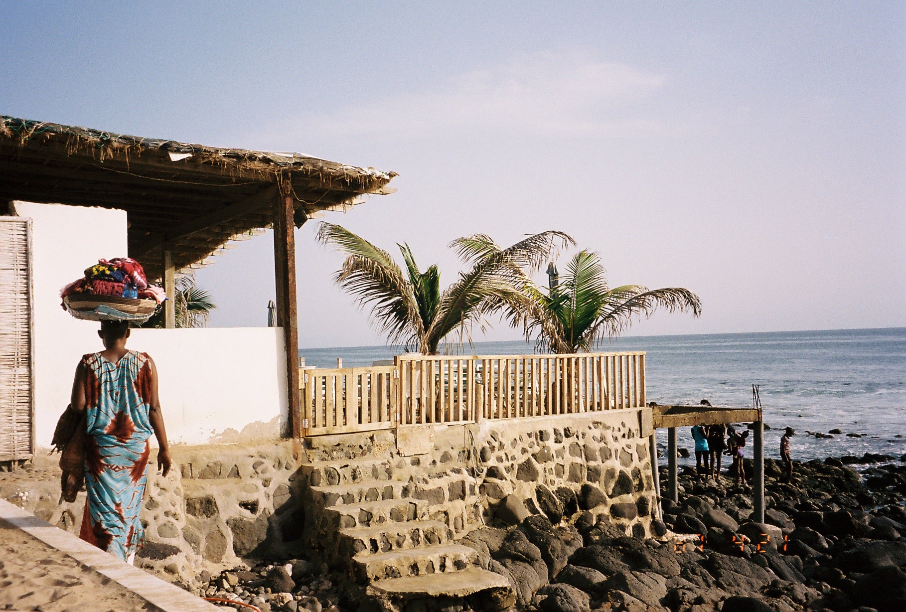 Photo d'une femme sénégalaise portant sur sa tête ses confections en tissus sur la plage